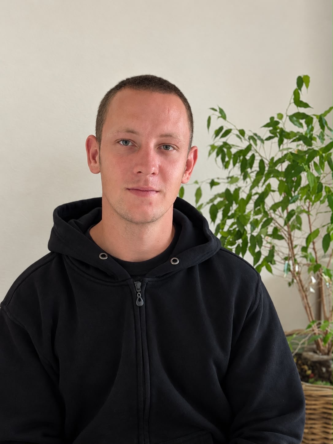 Jannik Münch in dunklem Pullover vor einer Zimmerpflanze